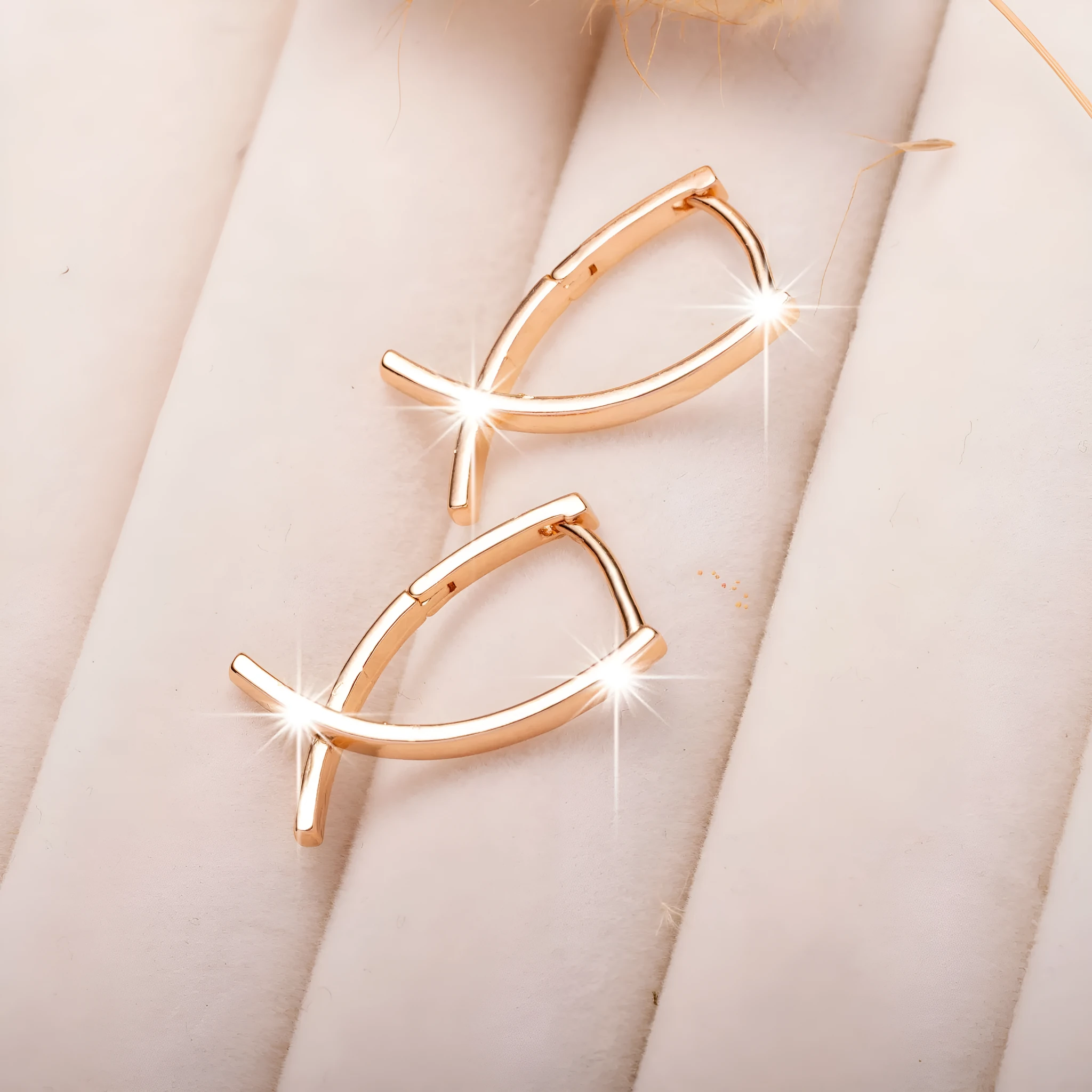 A pair of rose gold coloured cross shaped earrings made from copper on a plain background.