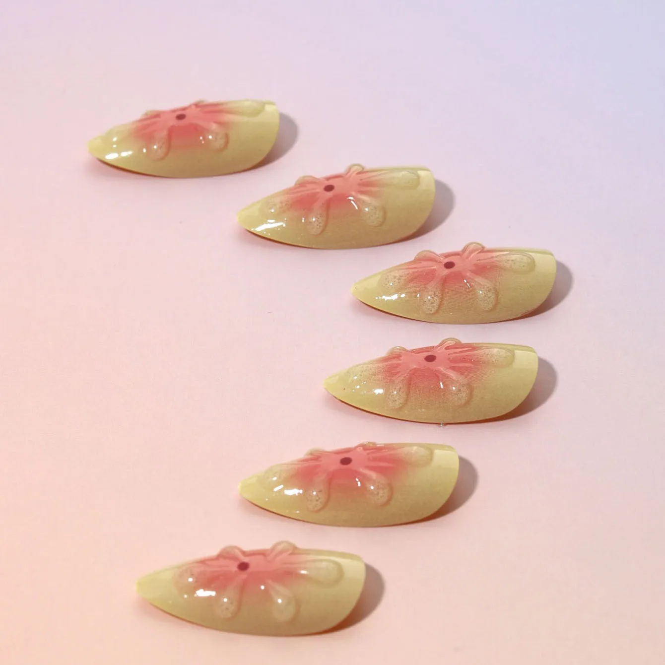Set of plastic fake nails with raised cartoon flower designs, jelly glue, and a nail file on a pink background.