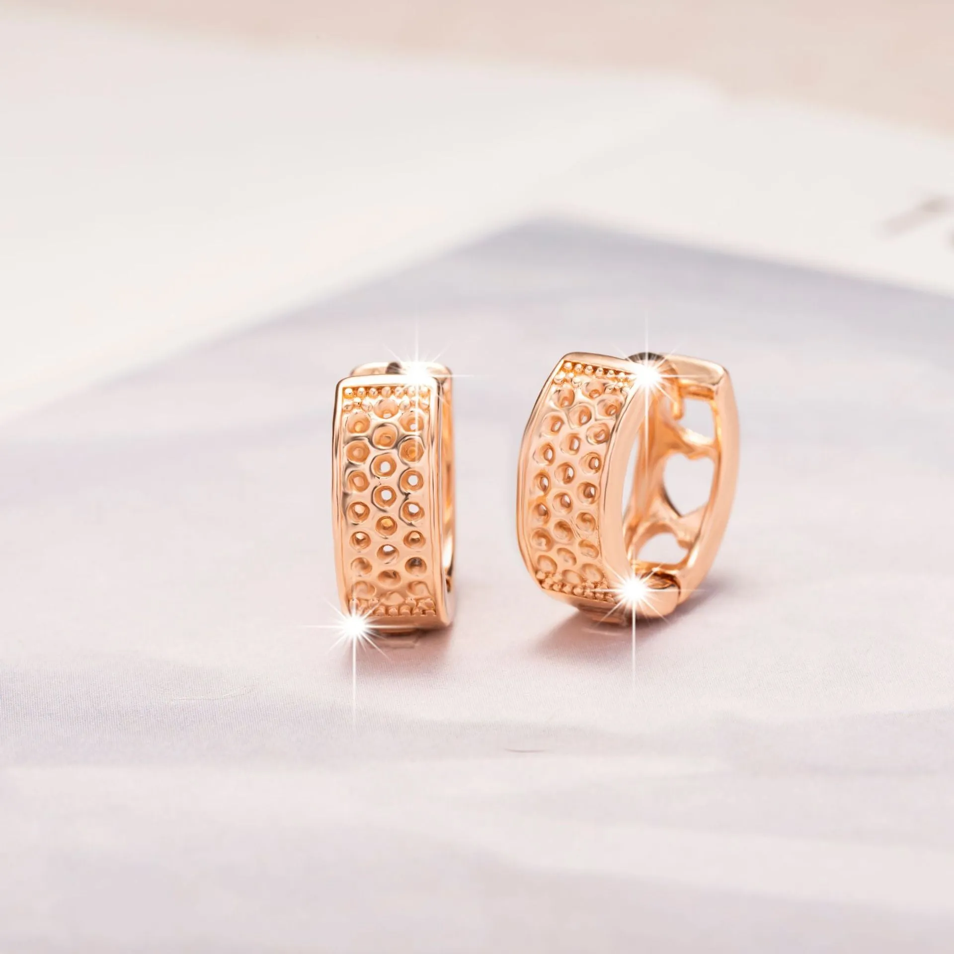 Rose gold circular earrings with three hollowed-out heart shapes.