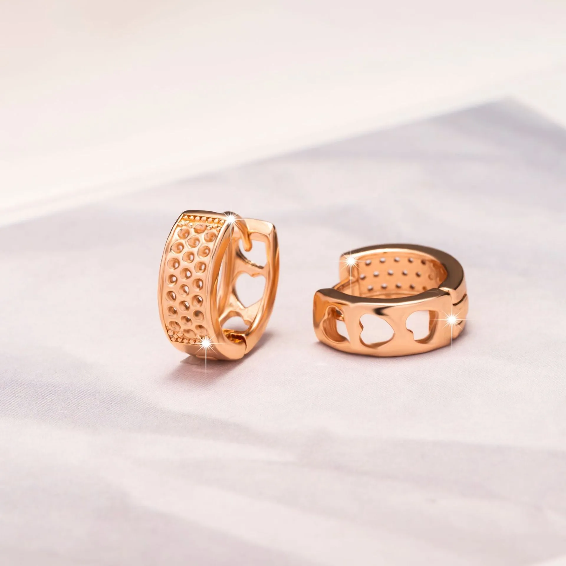 Rose gold circular earrings with three hollowed-out heart shapes.