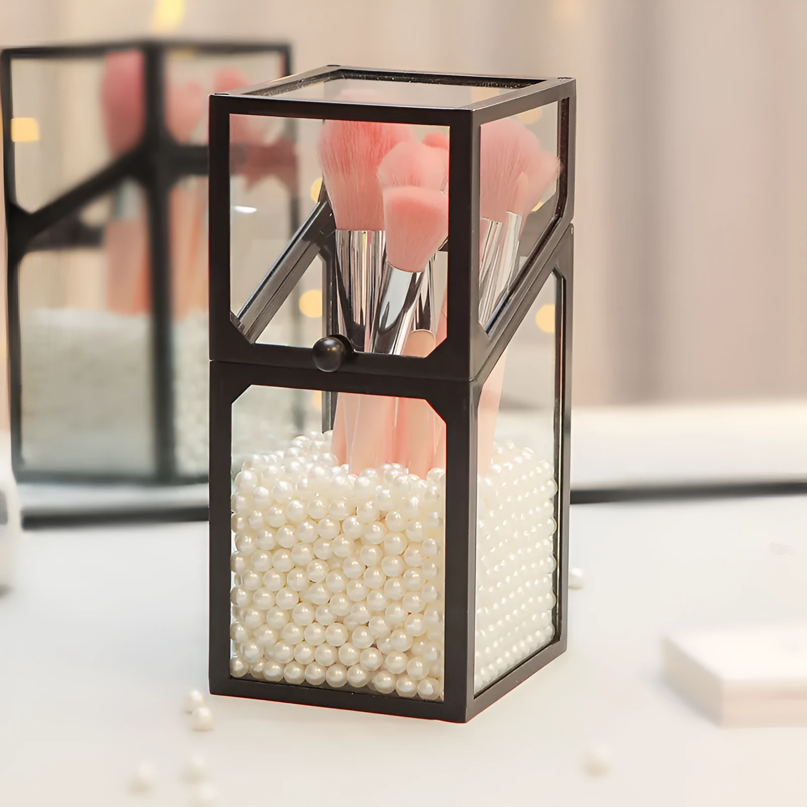Transparent glass makeup brush bucket with black lid on white surface showing brushes inside