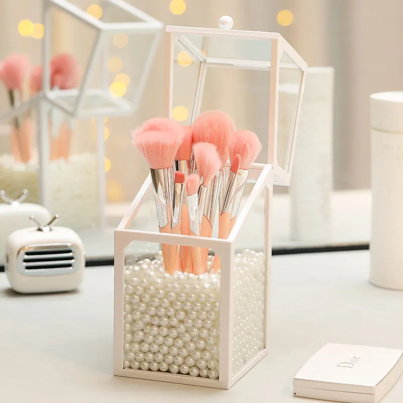 Transparent glass makeup brush bucket with black lid on white surface showing brushes inside