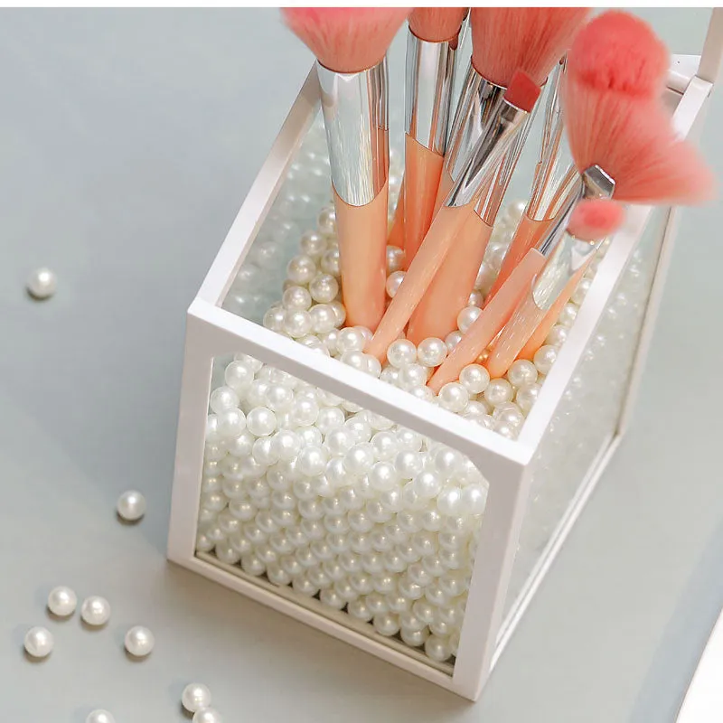 Transparent glass makeup brush bucket with black lid on white surface showing brushes inside