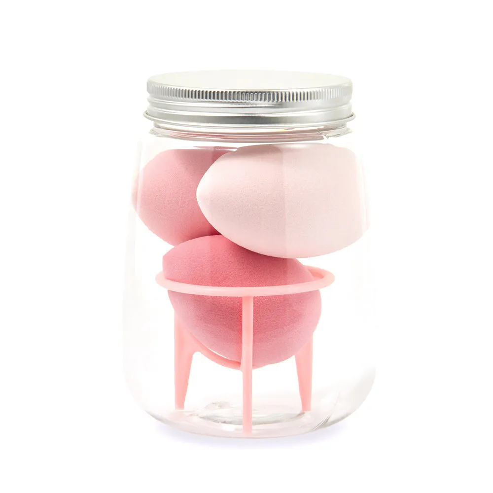 Three cosmetic sponges in different shapes placed on a holder next to a clear jar containing additional sponges.