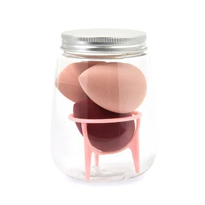 Three cosmetic sponges in different shapes placed on a holder next to a clear jar containing additional sponges.