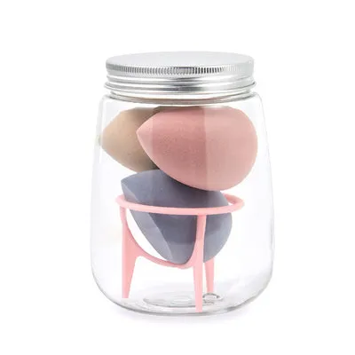 Three cosmetic sponges in different shapes placed on a holder next to a clear jar containing additional sponges.