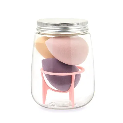 Three cosmetic sponges in different shapes placed on a holder next to a clear jar containing additional sponges.