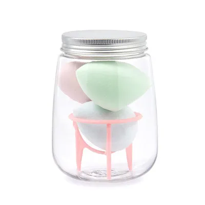 Three cosmetic sponges in different shapes placed on a holder next to a clear jar containing additional sponges.