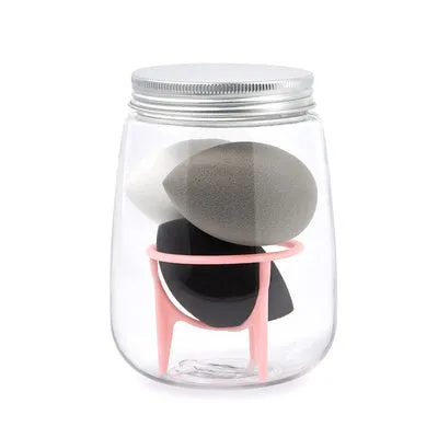 Three cosmetic sponges in different shapes placed on a holder next to a clear jar containing additional sponges.