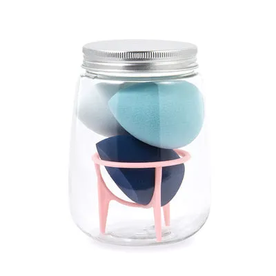 Three cosmetic sponges in different shapes placed on a holder next to a clear jar containing additional sponges.