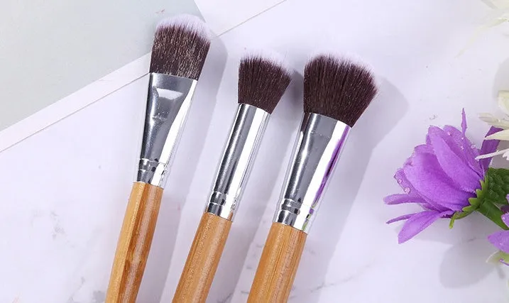 11 bamboo handle makeup brushes arranged on linen bag, including foundation blush and eye shadow brushes