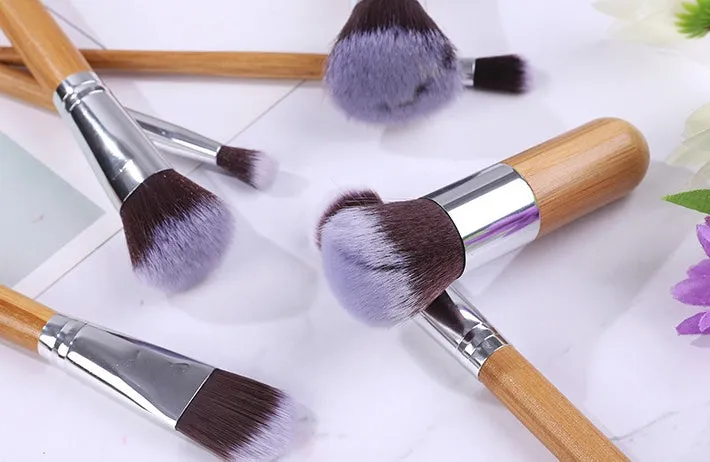11 bamboo handle makeup brushes arranged on linen bag, including foundation blush and eye shadow brushes