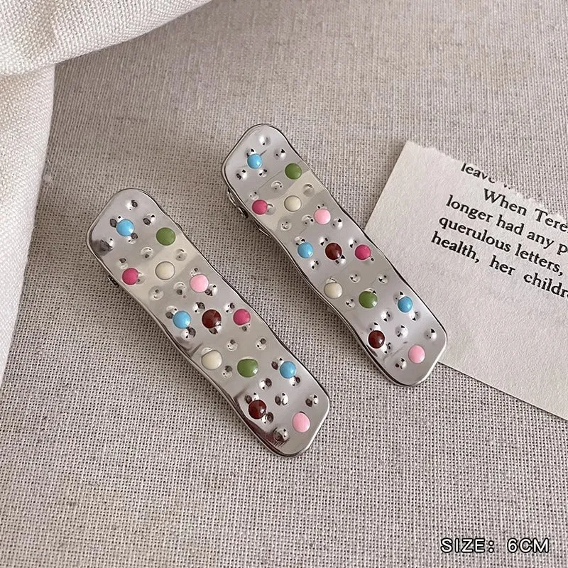 Two shiny silver metal duckbill barrettes with hollow star patterns on a plain background