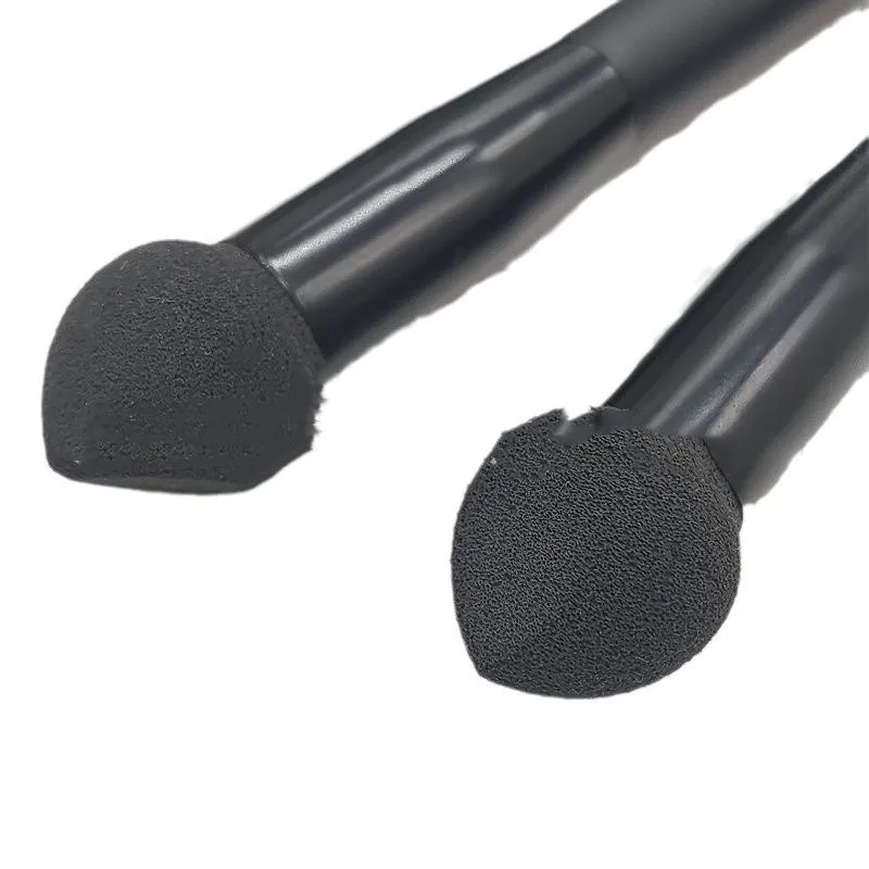 Black wooden handle concealer brush with a grey sponge tip applicator angled for under eye use.