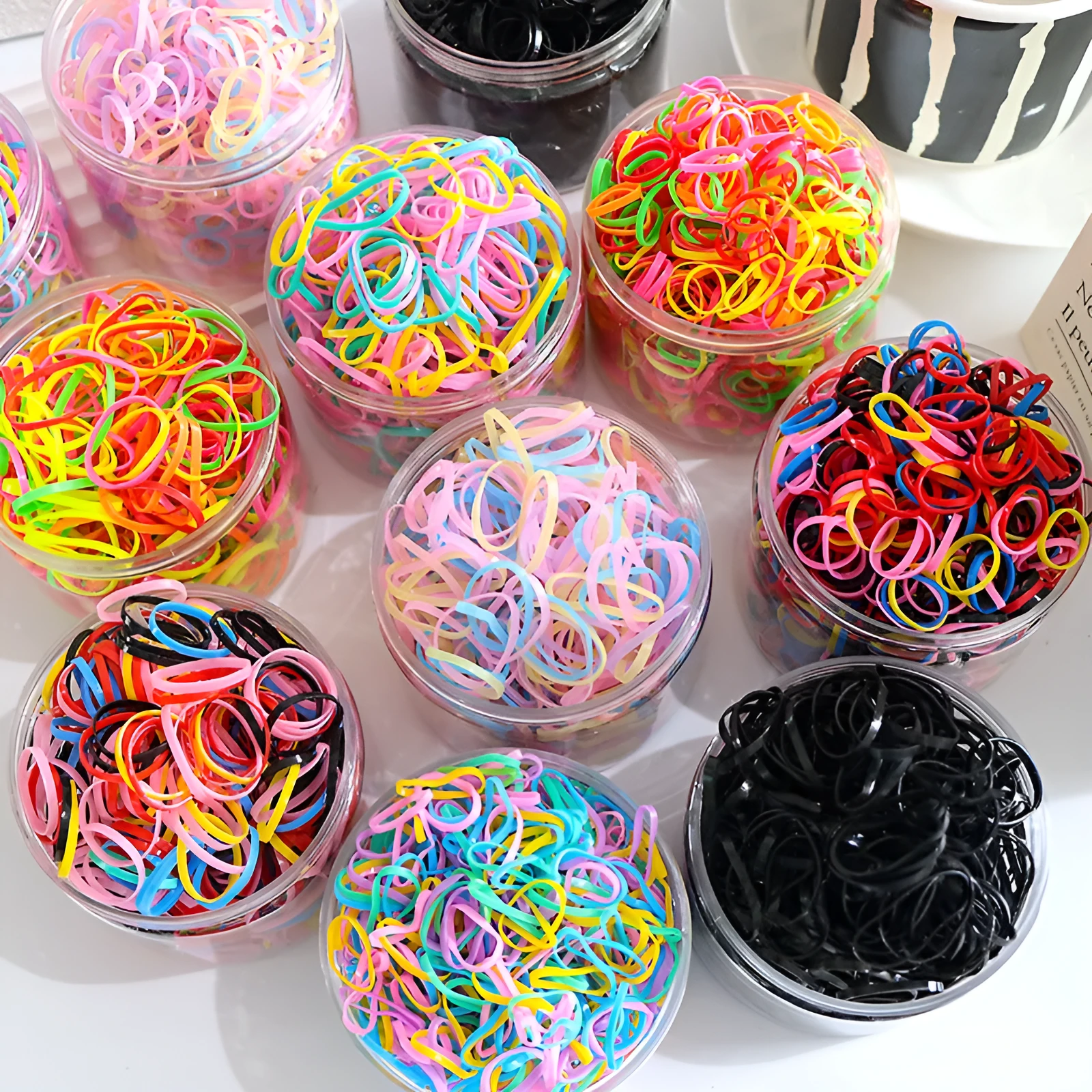 Multi-colour assortment of thin TPU baby hair ties in a re-useable plastic storage container.