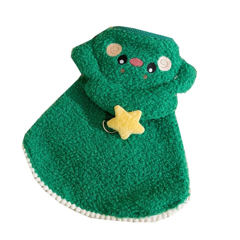 Cat wearing a green granular velvet Christmas cape with a star-topped tree hat, standing on a wooden floor