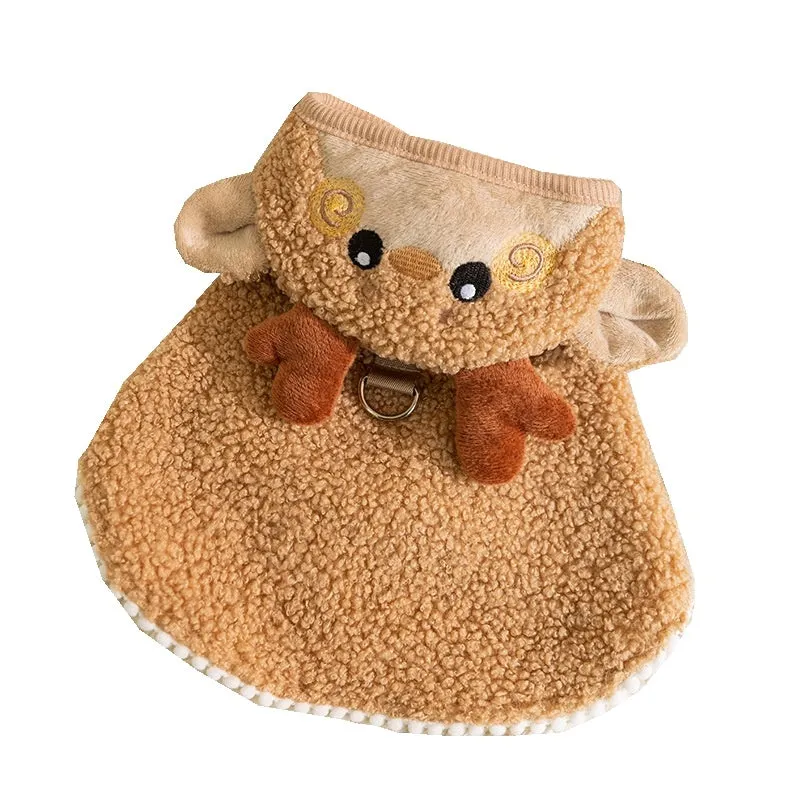 Cat wearing a green granular velvet Christmas cape with a star-topped tree hat, standing on a wooden floor