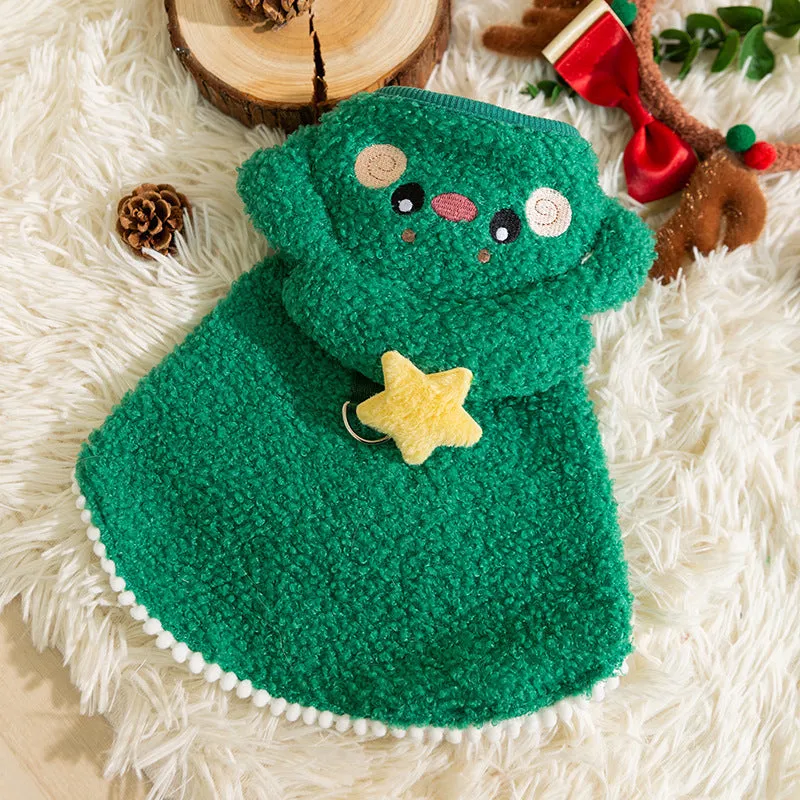 Cat wearing a green granular velvet Christmas cape with a star-topped tree hat, standing on a wooden floor