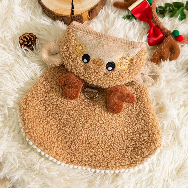 Cat wearing a green granular velvet Christmas cape with a star-topped tree hat, standing on a wooden floor