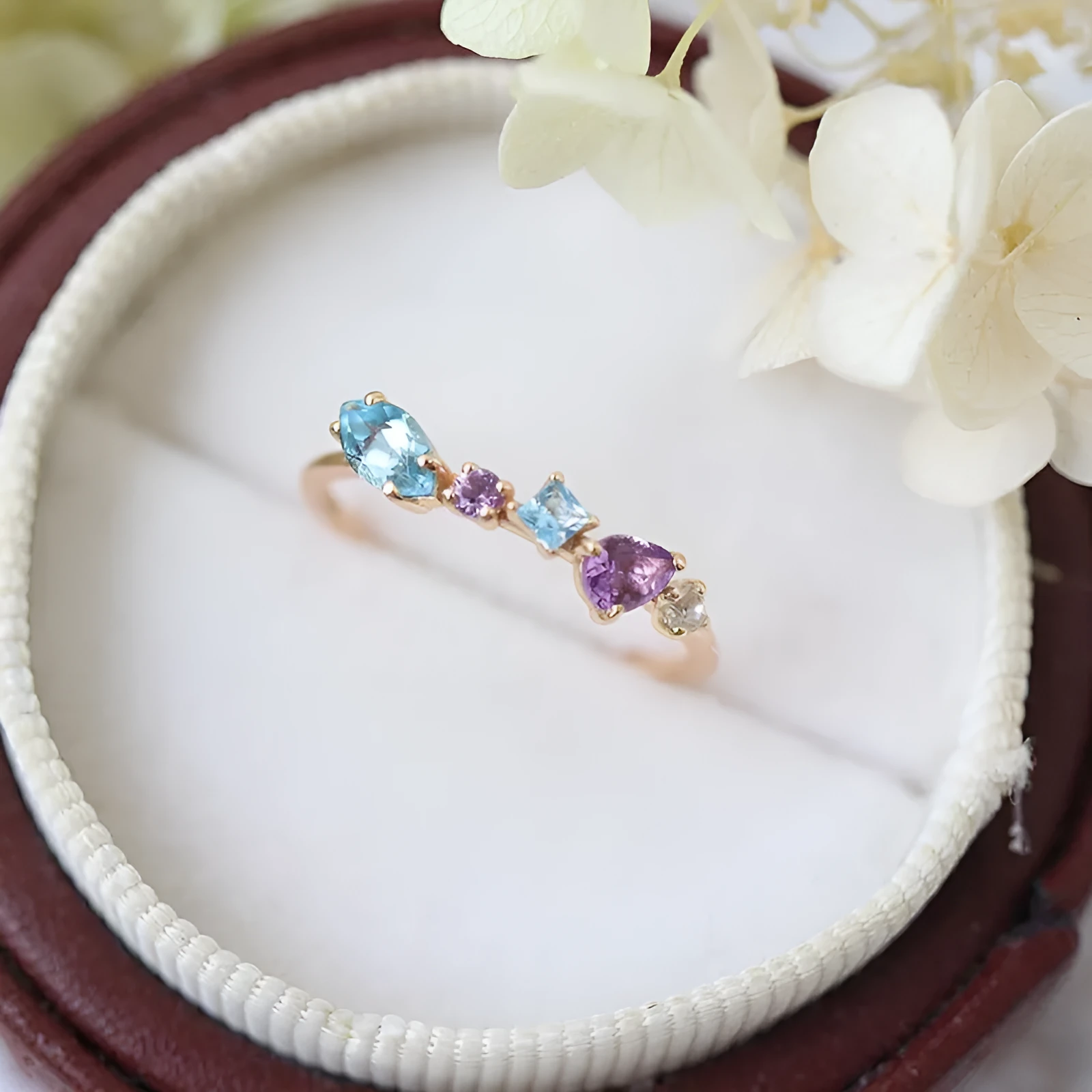 Gold-plated geometric ring with inlaid topaz and white amethyst stones on a white background