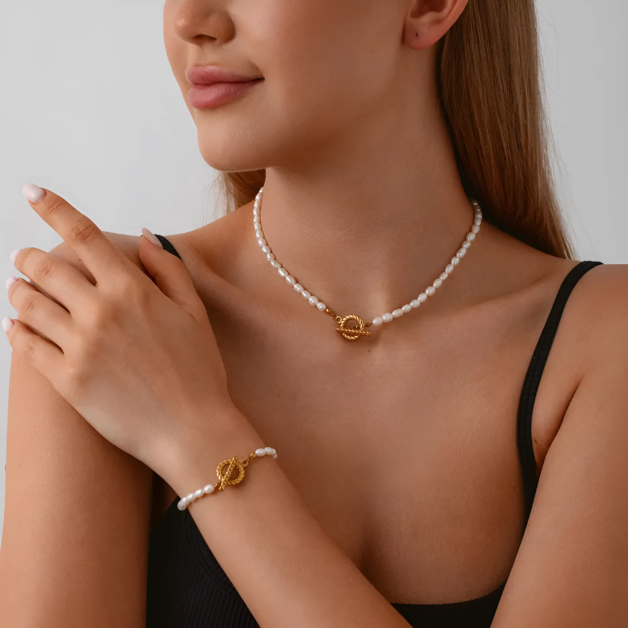 Women's freshwater pearl and geometric stainless steel necklace and bracelet set on a grey background
