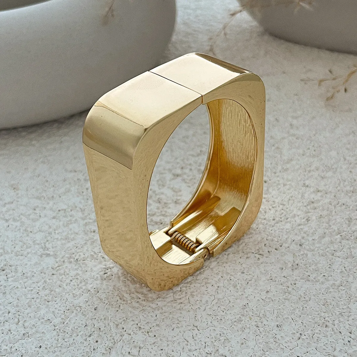 Metal texture glossy spring bracelet with geometric square mirror design in gold colour on white background