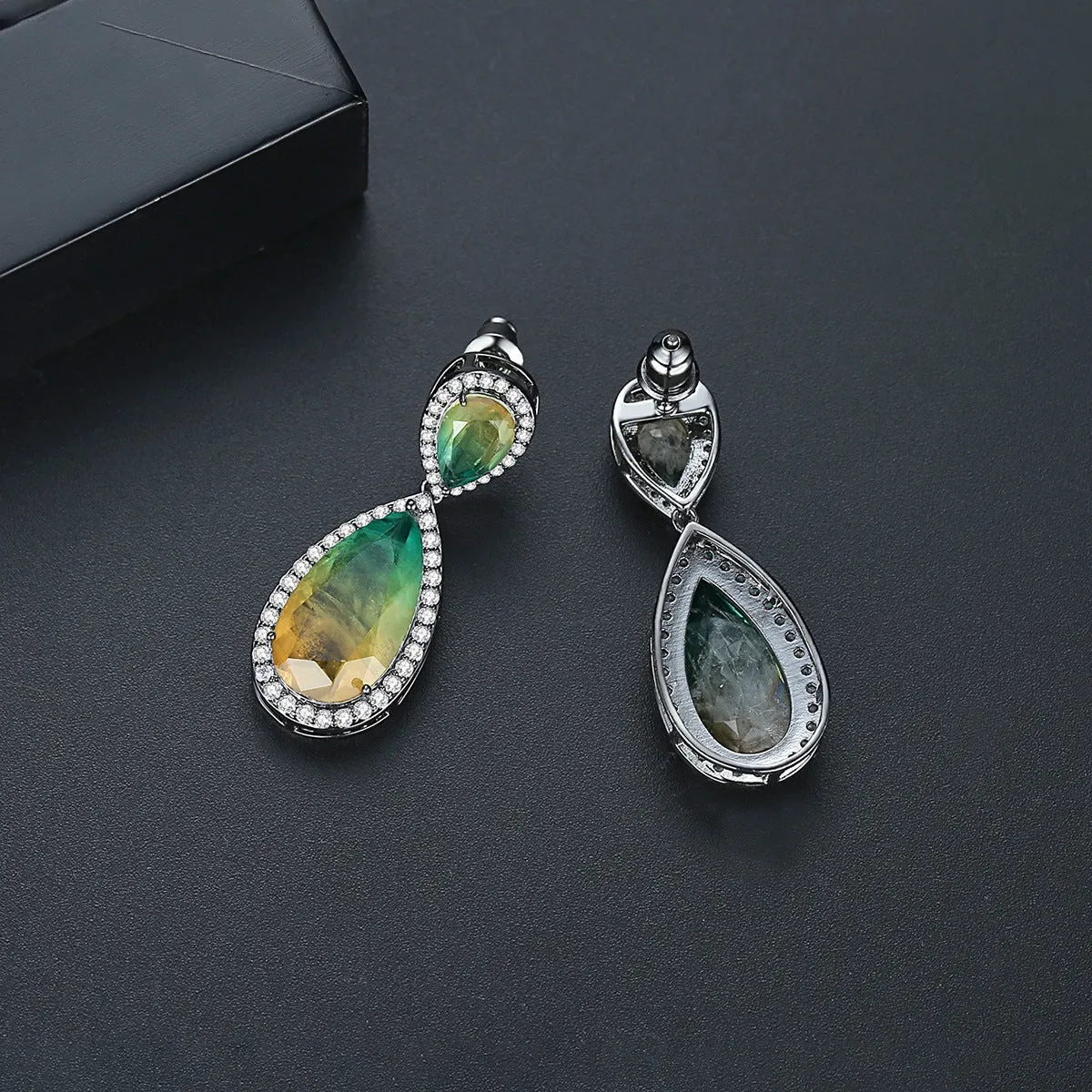 Drop shape copper earrings with inlaid synthetic gemstone in blue colour option on a white background