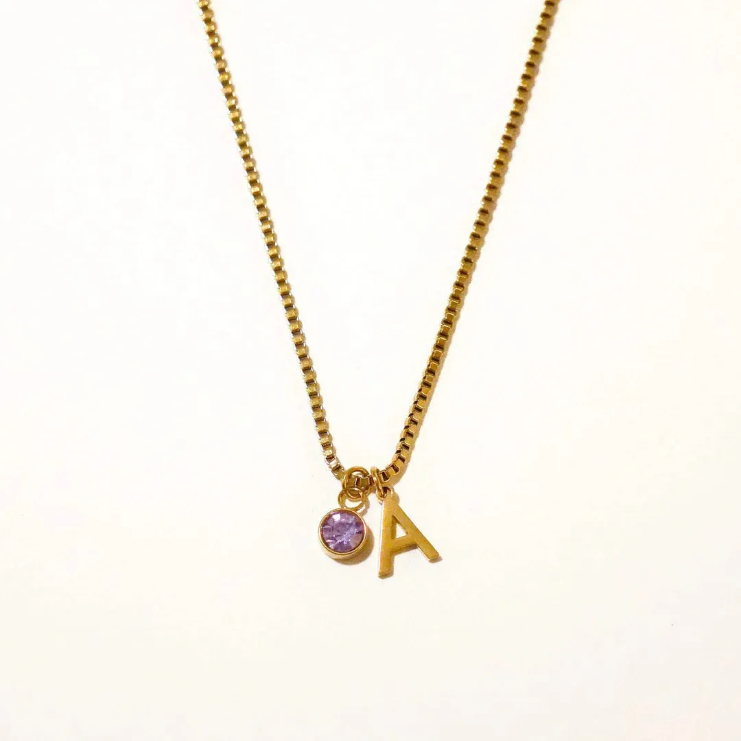 Gold coloured titanium steel birthstone initial pendant necklace with O-ring chain on white background