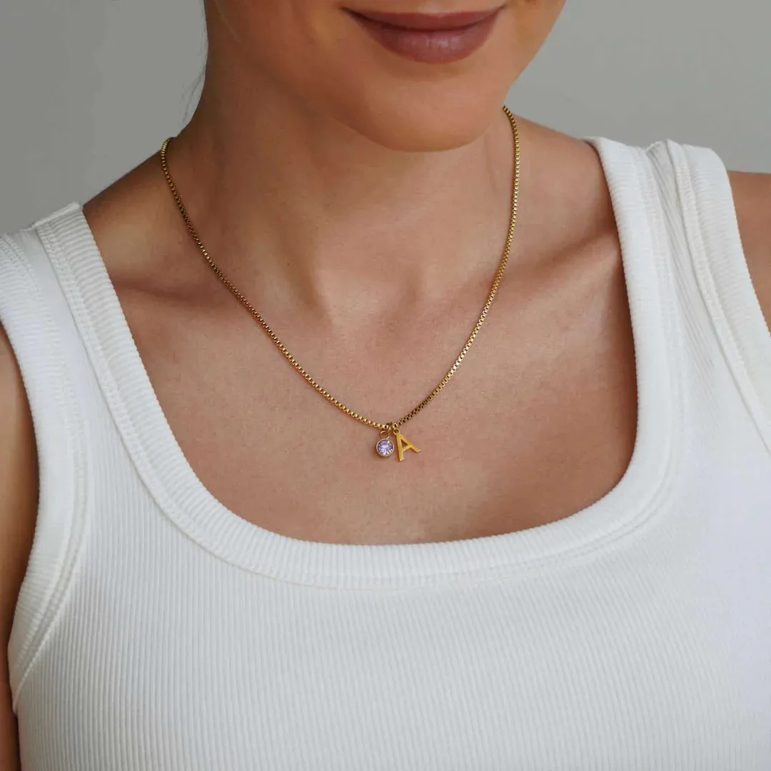 Gold coloured titanium steel birthstone initial pendant necklace with O-ring chain on white background