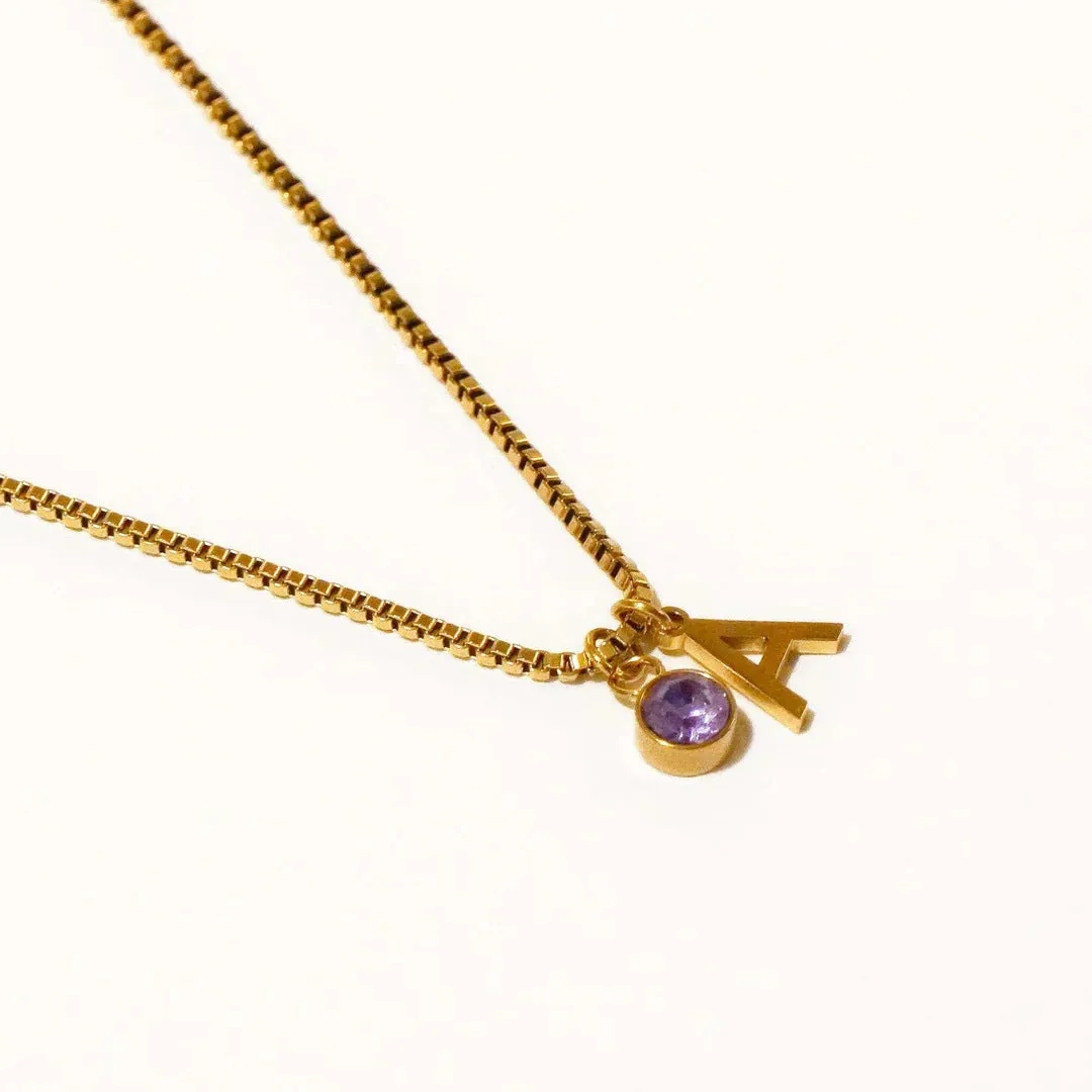 Gold coloured titanium steel birthstone initial pendant necklace with O-ring chain on white background