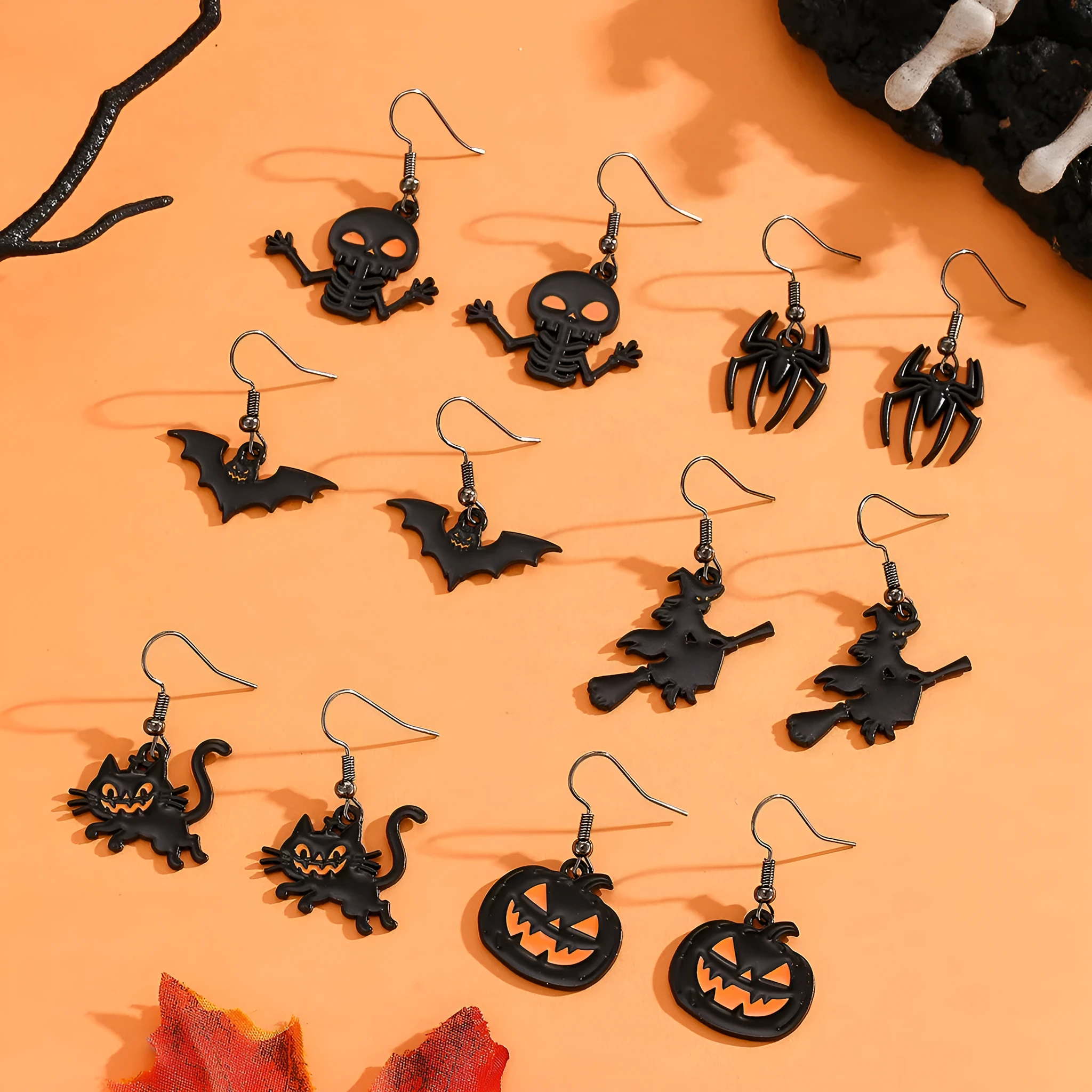 Set of six Halloween earrings with bat, cat, pumpkin head, skeleton, spider, and witch motifs on a dark background