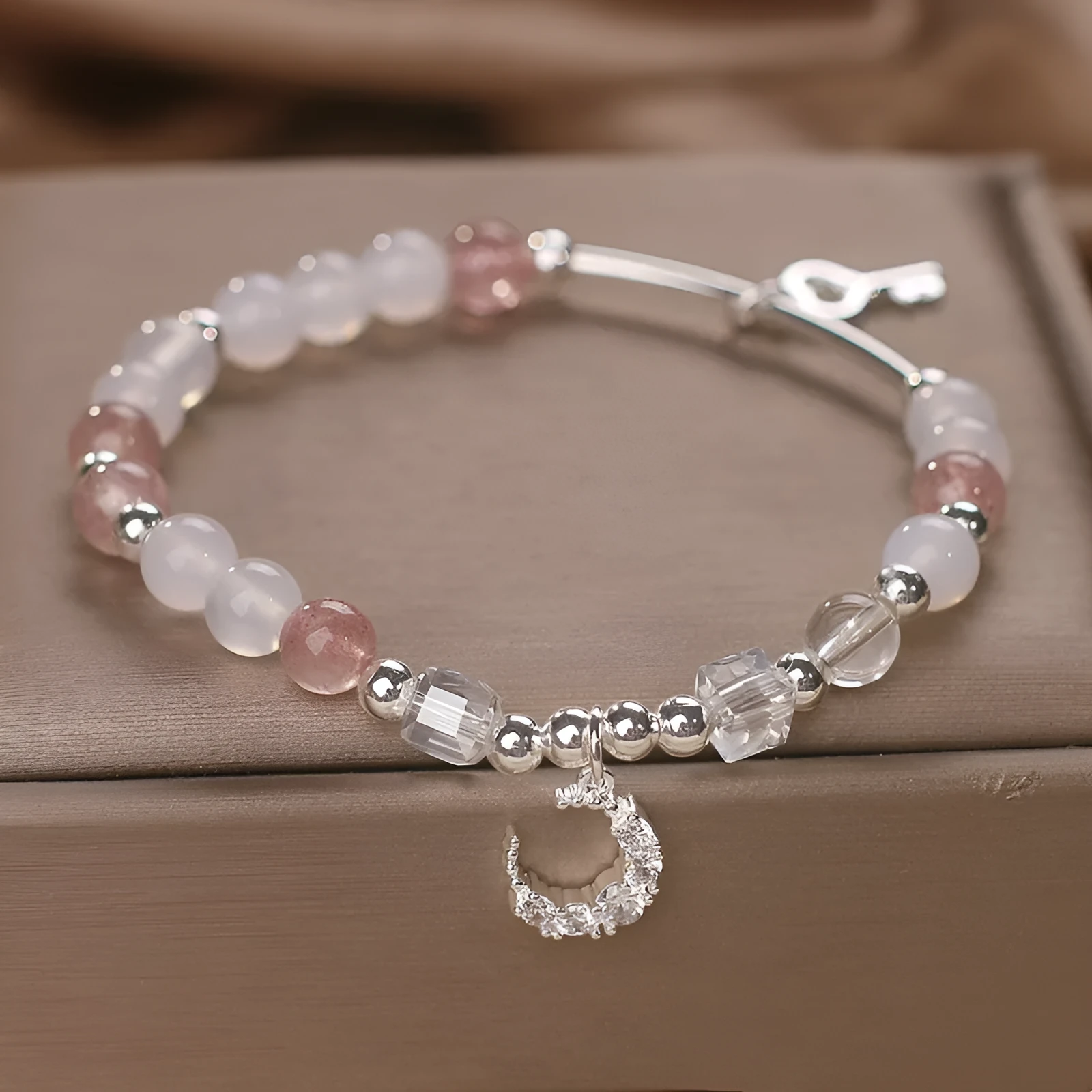 Natural strawberry quartz bracelet with pink cube sugar beads and moon pendant on a flat surface