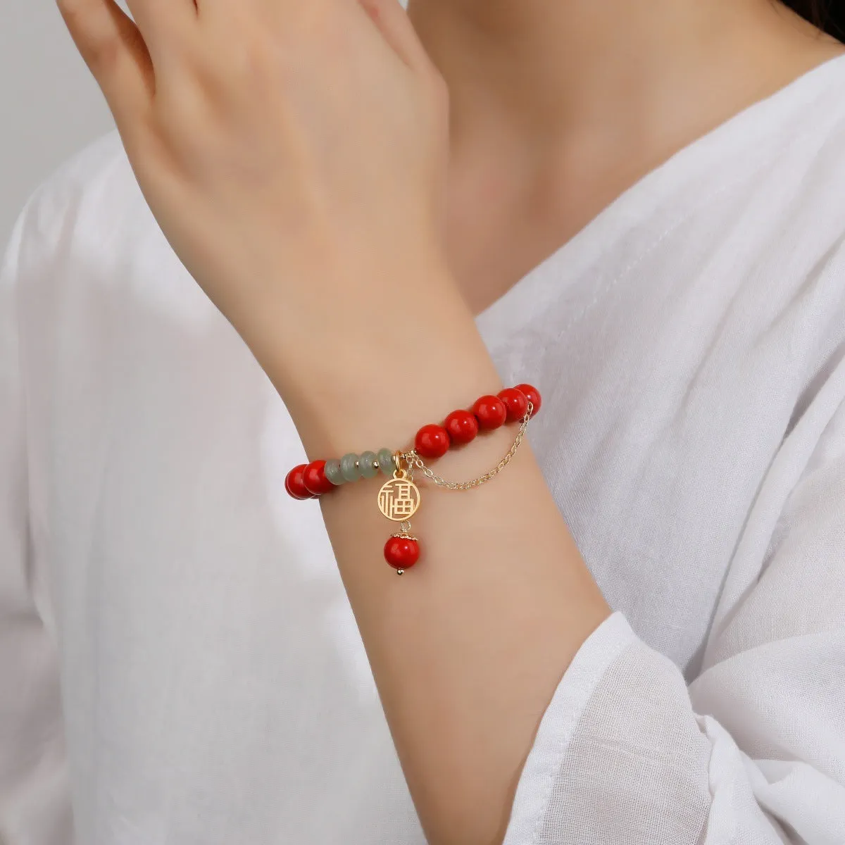 Women's red cinnabar bracelet with fu character charm, jade spacer bead, and tassel design