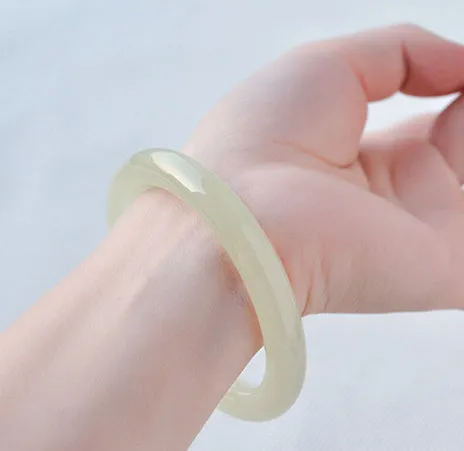 Round bar jade bracelet with a winding silk pattern on a plain background.