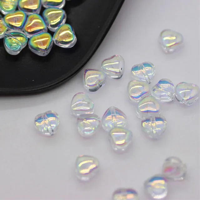 Twenty transparent love heart shaped spacer beads in assorted colours on a white background.