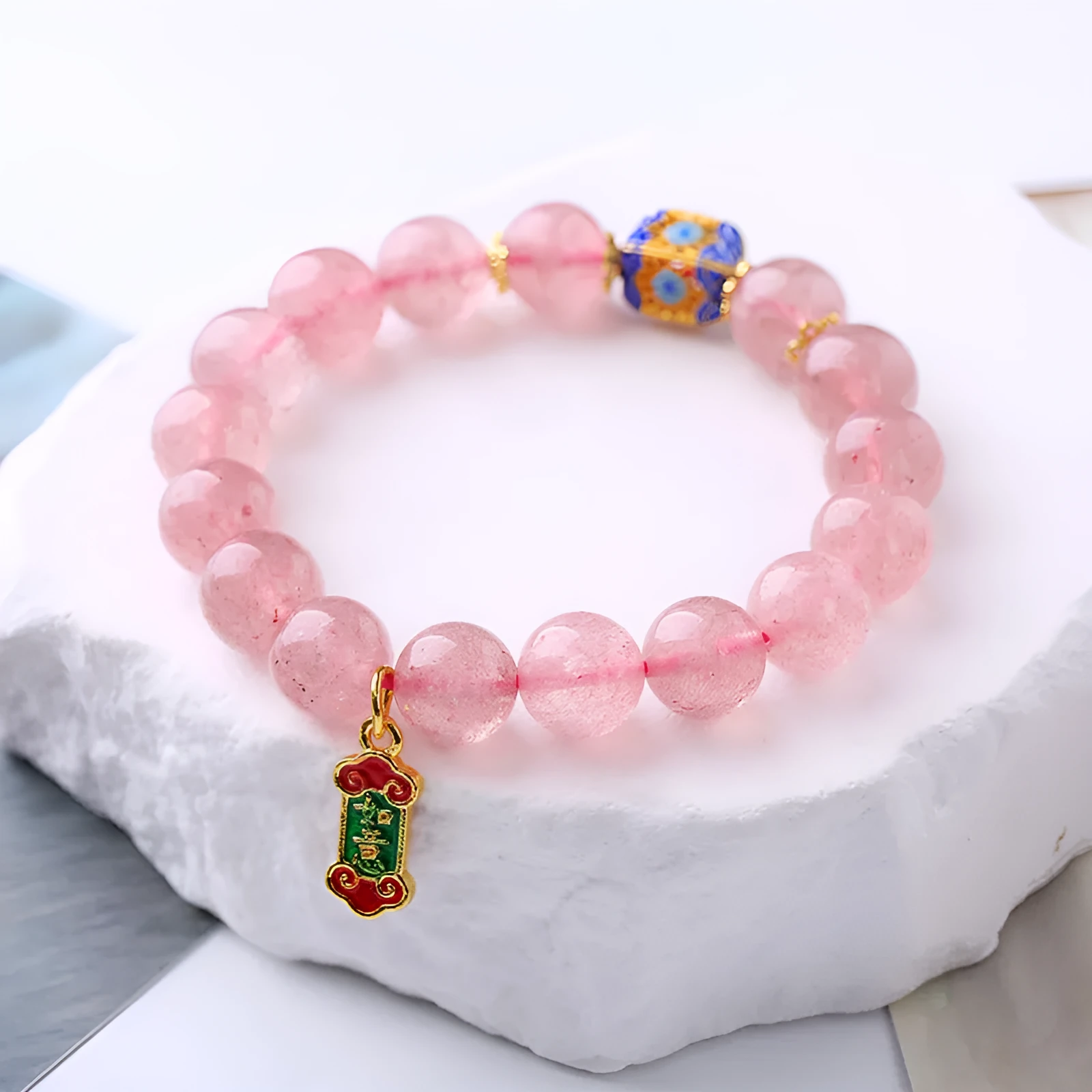 Close-up of a pink crystal bracelet with a Ruyi charm and text detailing on a woven chain.