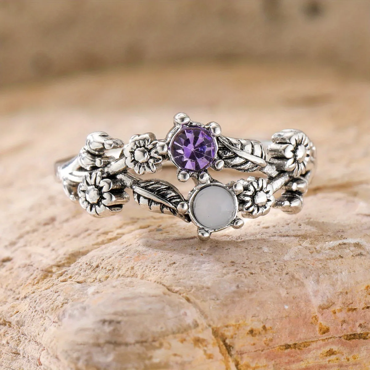 Silver zinc alloy flower ring with purple gemstone centre on light background
