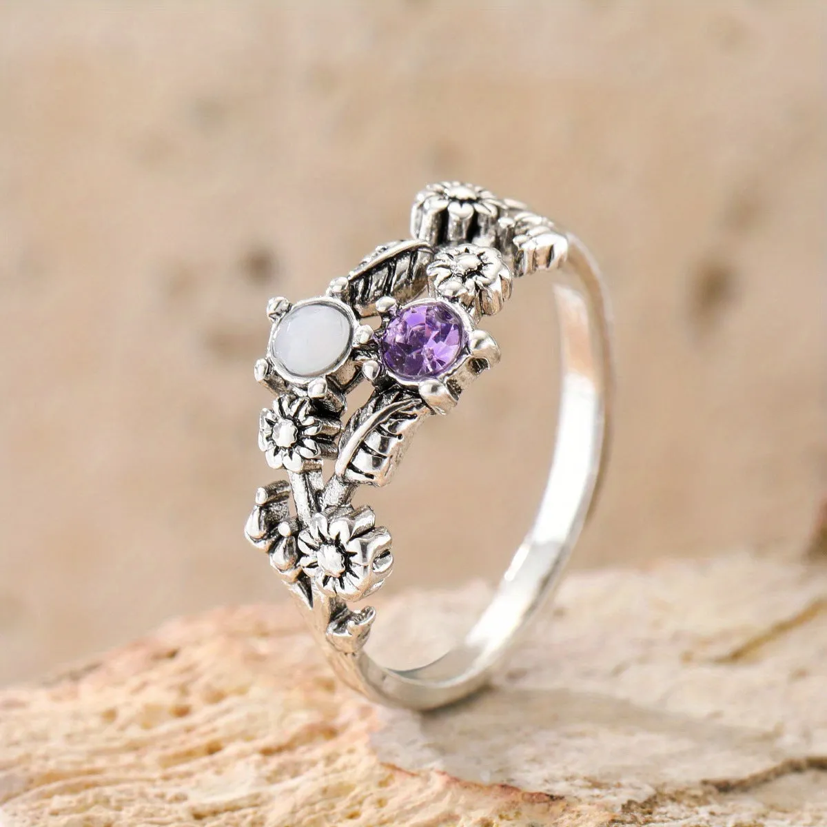 Silver zinc alloy flower ring with purple gemstone centre on light background