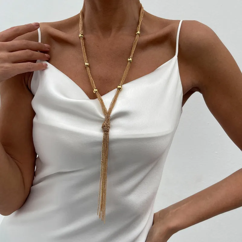 Simple Y-shaped metal tassel necklace set with gold finish and matching earrings on white background