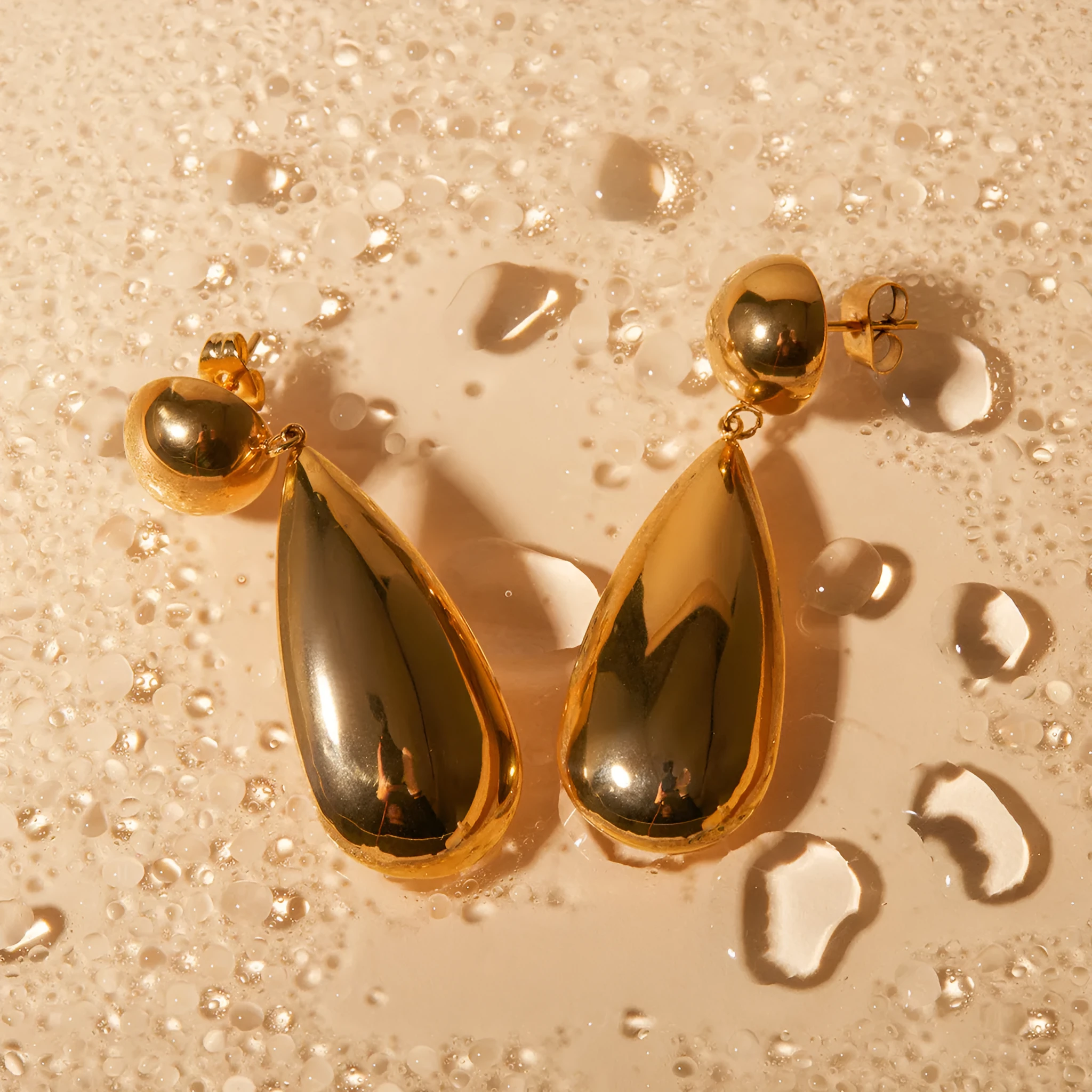 Gold coloured stainless steel earrings with a geometric hemisphere and water drop pendant design.