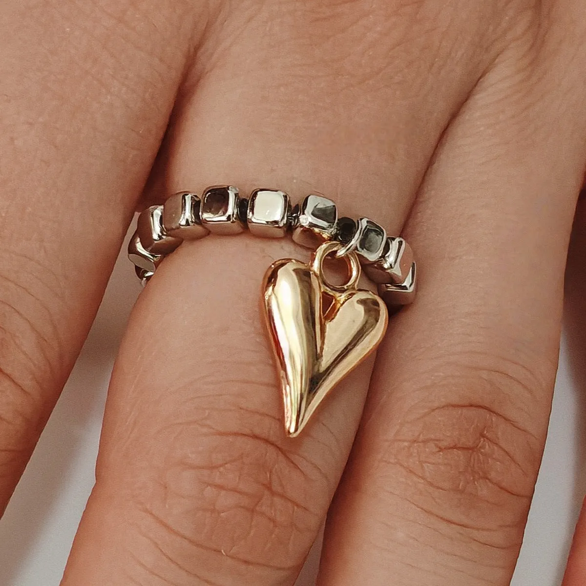 Handmade elastic love ring with geometric beaded string design and heart charm on adjustable band