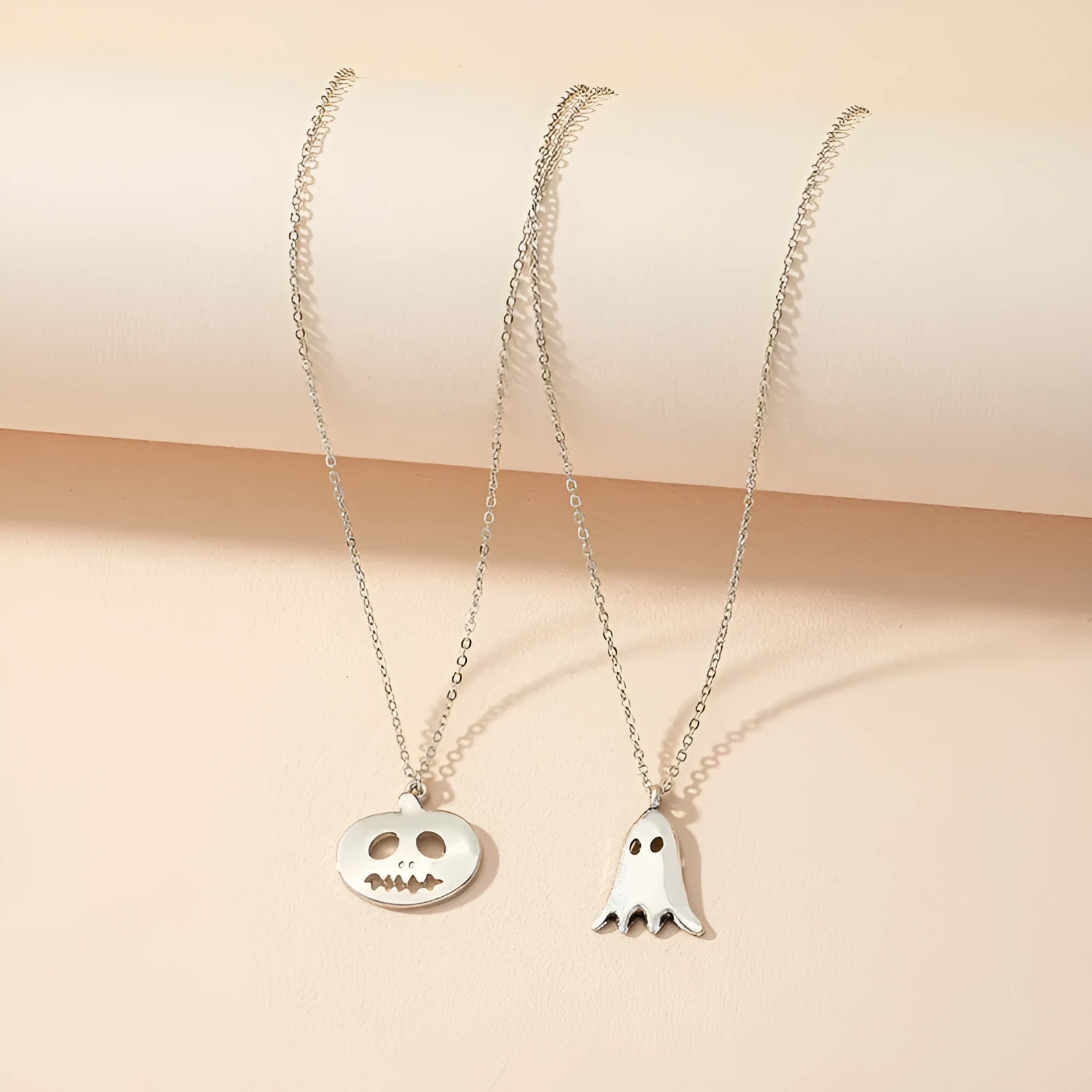 Two silver alloy pendant necklaces: one cartoon pumpkin and one cartoon ghost on a light background