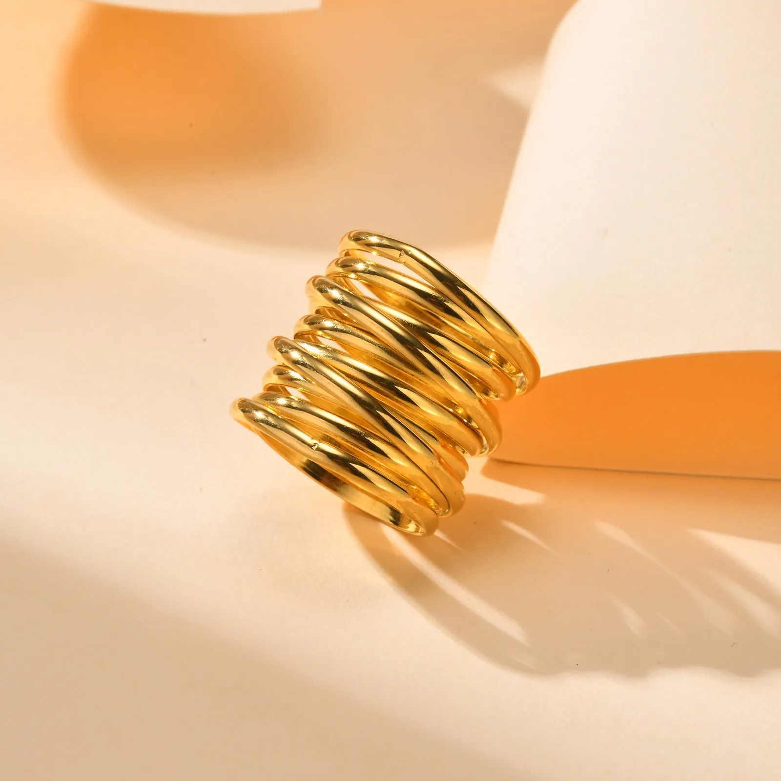 Gold stainless steel multi-loop multi-layer ring on a plain background