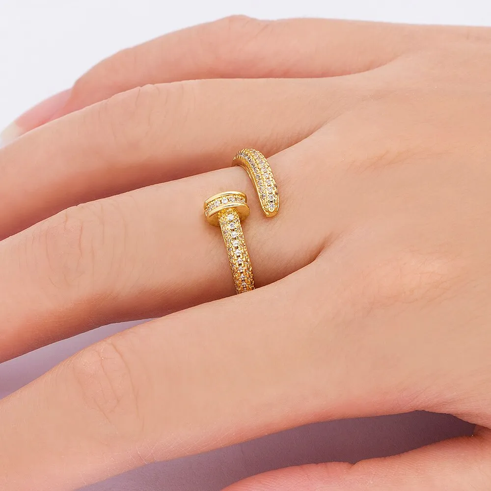Close-up of a gold plated geometric nail ring with inlaid drill details on a metallic surface.