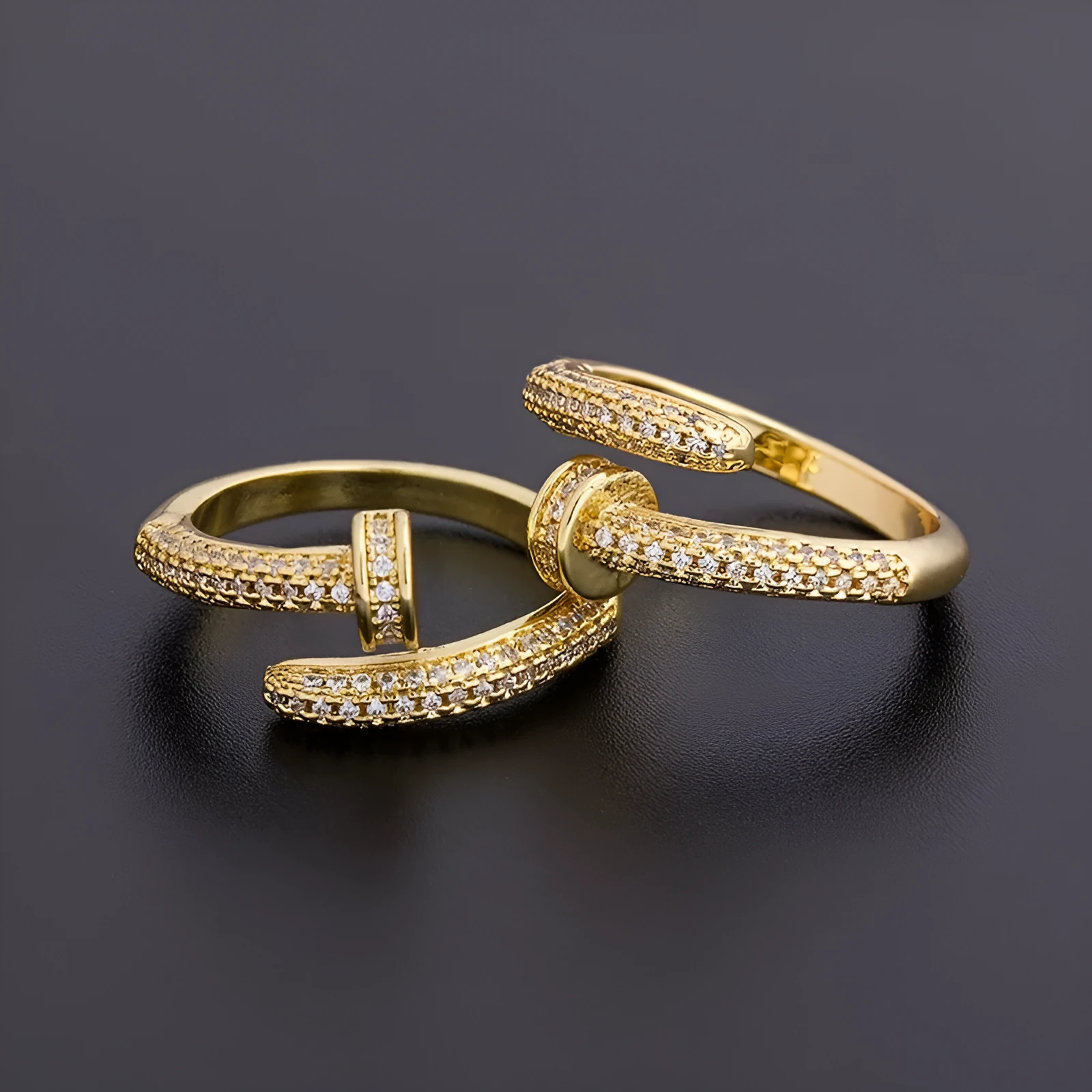 Close-up of a gold plated geometric nail ring with inlaid drill details on a metallic surface.