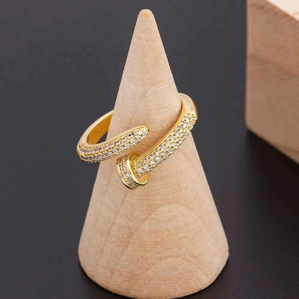 Close-up of a gold plated geometric nail ring with inlaid drill details on a metallic surface.