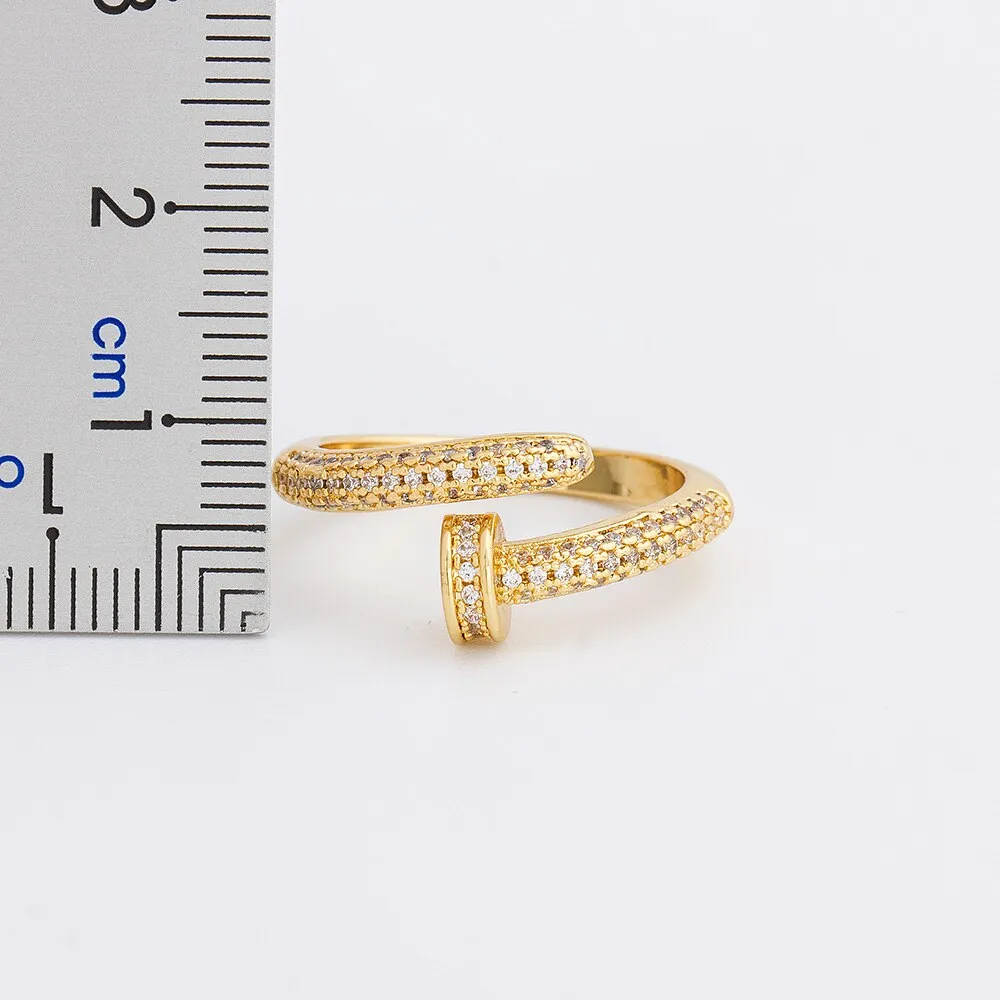 Close-up of a gold plated geometric nail ring with inlaid drill details on a metallic surface.