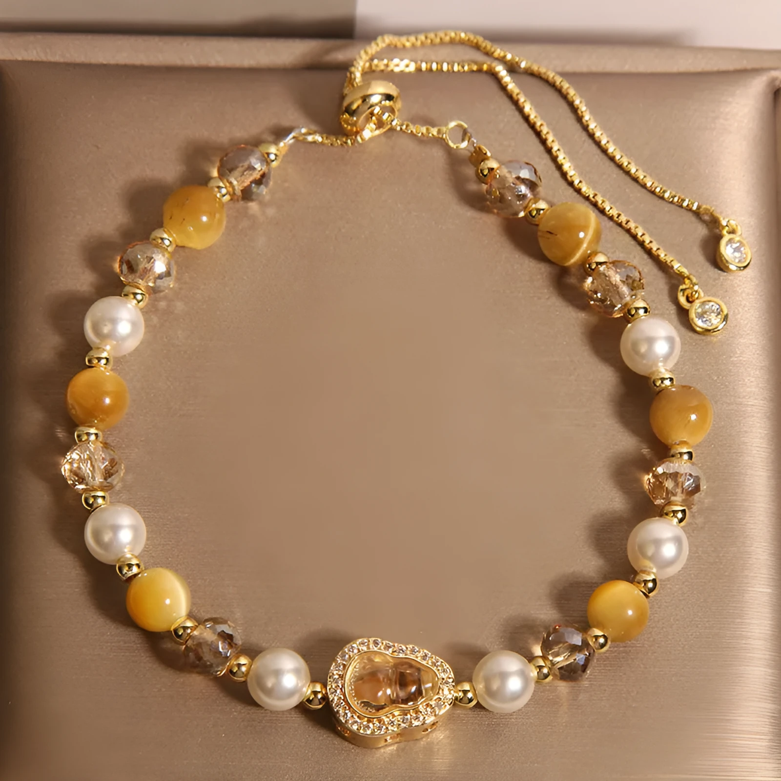 Yellow tiger's eye glass gourd pendant bracelet with alloy inlay and stone accents on a wrist.