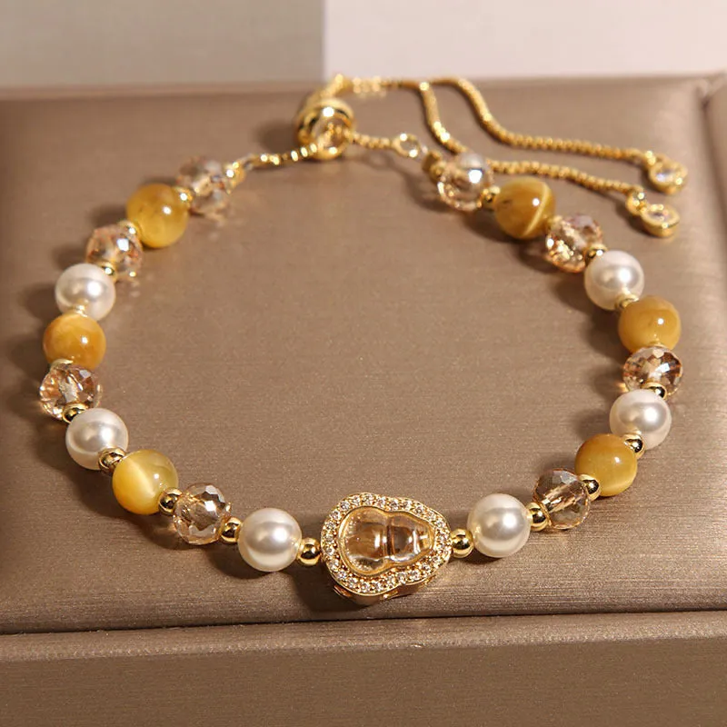 Yellow tiger's eye glass gourd pendant bracelet with alloy inlay and stone accents on a wrist.