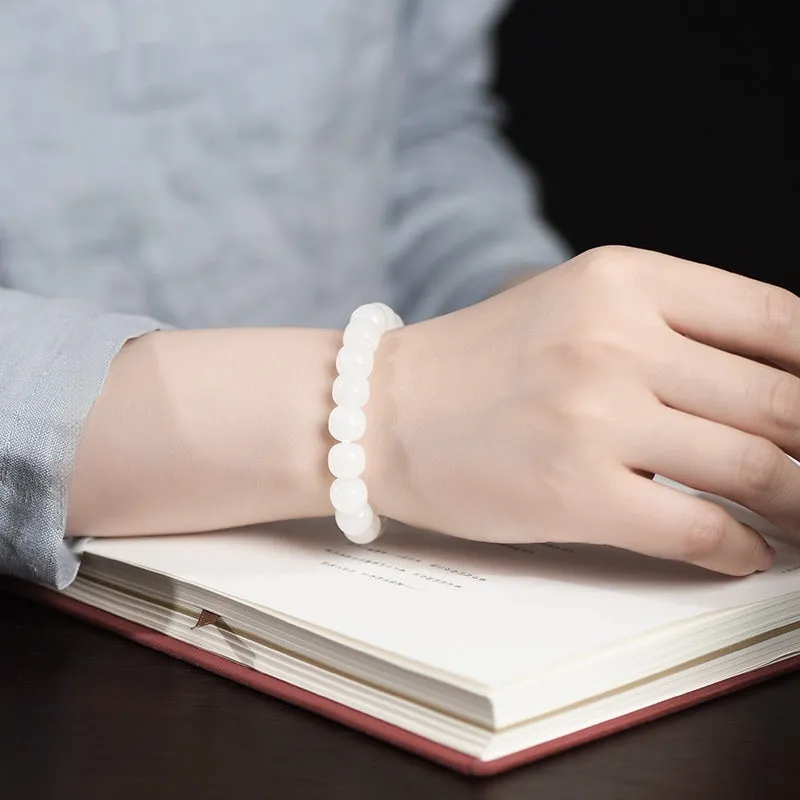 White Hetian jade barrel bead bracelet for men and women on a wooden surface.